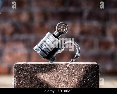 Vintage Barrel Padlock with screw key resting on brick with brick background on timber floorboards Stock Photo