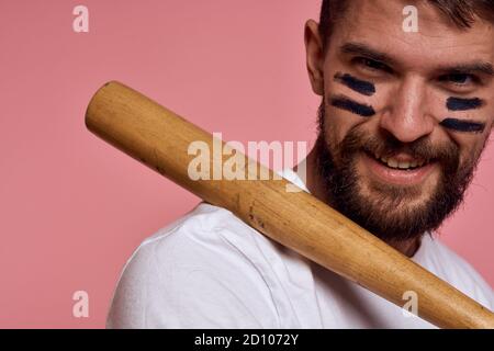 Emotional man with a baseball bat in his hand on a pink background and black lines on the face of the model grimace Stock Photo