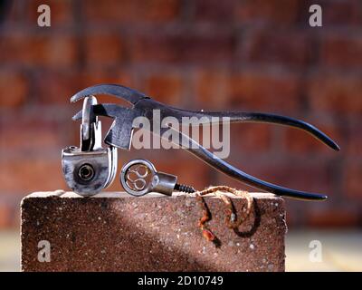 Vintage Barrel Padlock with screw key and vintage cobblers pliers resting on brick with brick background on timber floorboards Stock Photo