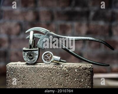 Vintage Barrel Padlock with screw key and vintage cobblers pliers resting on brick with brick background on timber floorboards Stock Photo