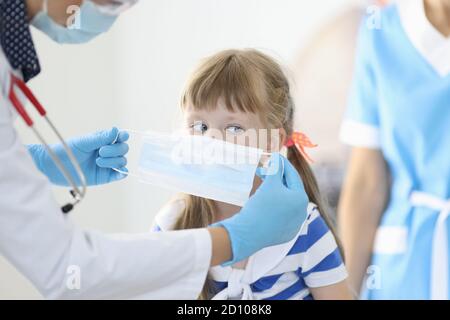 Doctor in white coat and with stethoscope put on protective mask for child. Stock Photo