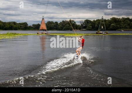 Young pretty slim brunette woman riding wakeboard on in a summer lake. Wakeboarding on cable Stock Photo