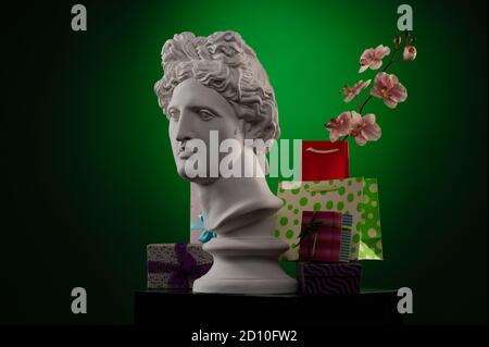 Statue of Apollo Belvedere, flowers and gifts boxes and packages, spotlights and multi-colored backgrounds. Stock Photo