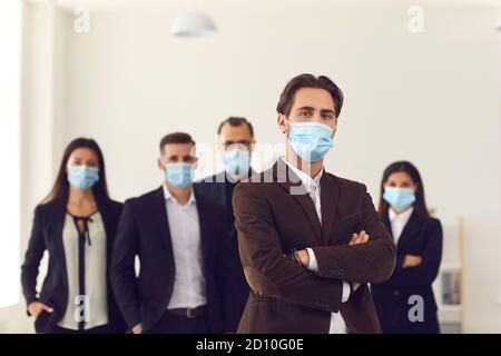 Male leader and team of responsible young company workers all wearing face masks at work Stock Photo