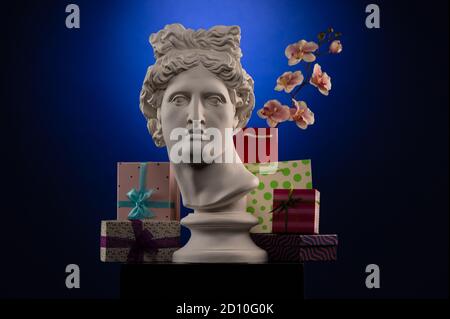 Statue of Apollo Belvedere, flowers and gifts boxes and packages, spotlights and multi-colored backgrounds. Stock Photo