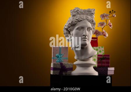 Statue of Apollo Belvedere, flowers and gifts boxes and packages, spotlights and multi-colored backgrounds. Stock Photo