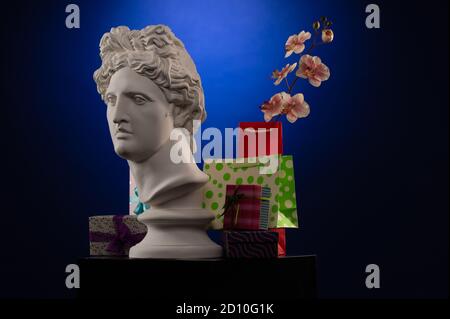 Statue of Apollo Belvedere, flowers and gifts boxes and packages, spotlights and multi-colored backgrounds. Stock Photo