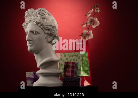 Statue of Apollo Belvedere, flowers and gifts boxes and packages, spotlights and multi-colored backgrounds. Stock Photo