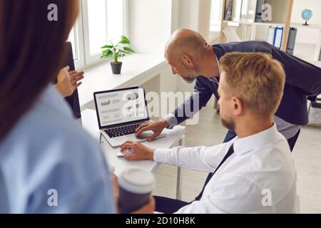 Workers analyze data statistics on a laptop by pointing to a screen displaying graphs and charts. Stock Photo