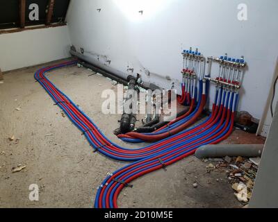 A portrait of a room under construction with a central heating collector on the wall. The warm and cold water tubes are running across the floor toget Stock Photo