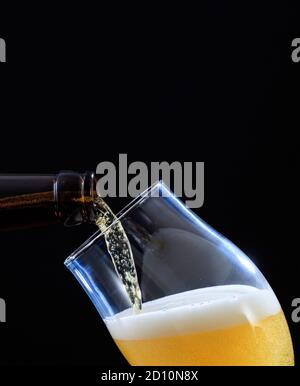 Beer bottle pouring golden ale beer in a glass, black backgrounnd, closeup cropped portrait view, copy space Stock Photo