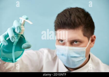 man in medical protective mask with antibacterial antiseptic gel for hand disinfection on blue background Stock Photo