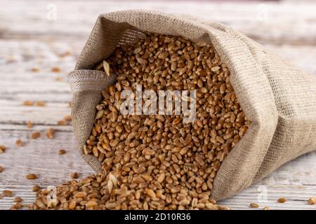 A sack of wheat grains on a wooden background. Natural flour products for baking bread and other pastries. Stock Photo