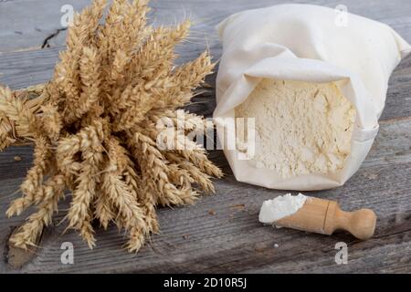 Flour sack, ears and wooden measuring cup on wooden background. Natural baking products. Stock Photo