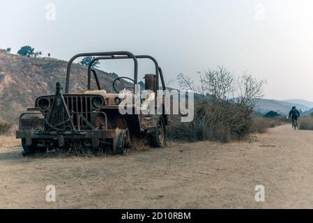 Old 1928 jeep body rusted and stripped flat tires with hiker walking in the background on the trail. Stock Photo