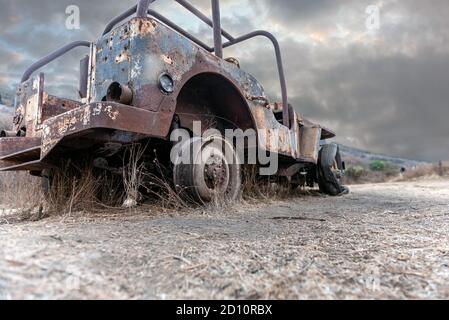 Old 1928 jeep body rusted and stripped flat tires broken down along the side of hiking trail with overcast clouds in the sky. Stock Photo