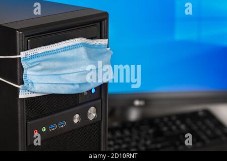 Coronavirus and antivirus protection concept. Computer weared in protective face mask. Desktop PC with copy space on monitor detail. Online home work. Stock Photo