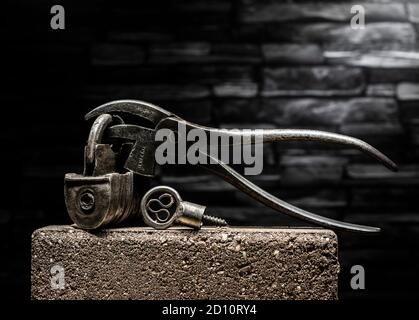 Vintage 1800's Barrel Padlock with screw key and vintage cobblers pliers against slate background Stock Photo