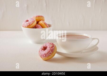 Mug of hot cocoa and donuts on white background. Tasty pink donuts and hot cacao cup. Sweet breakfast Stock Photo