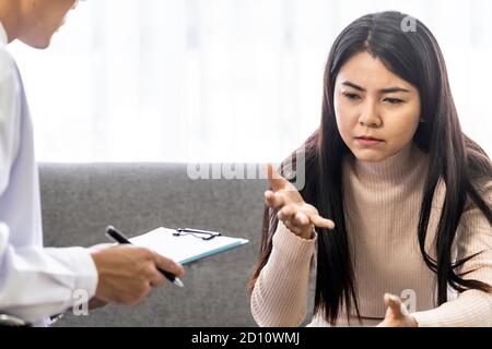 Portait of asian female patient talking to Psychotherapist doctor in medical clinic for consult about her mental health after stress strain from quara Stock Photo