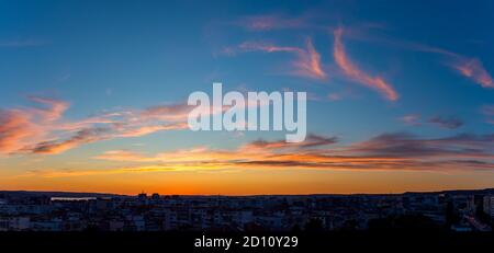 Panoramic shot of golden blue twilight sky with orange pink clouds over a small city. Scenic skyscape just after the sun goes down over the horizon. Stock Photo