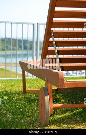 Close up of exterior wooden deck chair on lawn. View of beauriful nature and lake visible through fence. Stock Photo