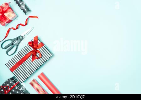 Gift boxes wrapped in black and white striped, dotted and red paper with wrapping materials over a blue background. Various designes wrapped presents Stock Photo