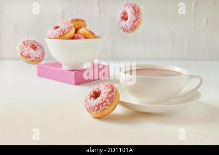 Flying pink donuts with a cup of cacao on a white background. selective focus on pink flying donuts Stock Photo
