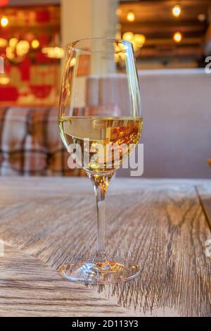 A glass of white wine stands on a table with a wooden surface in a cafe. Vertical orientation, selective focus, blurred background. Stock Photo