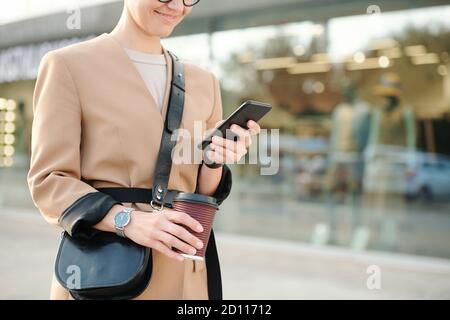 Young smiling woman with drink and handbag scrolling through contacts or texting Stock Photo
