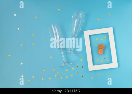 Two crystal champagne glasses and white frame withbottle cork on blue background with confetti. Christmas drinks. Celebrating Christmas. Horizontal or Stock Photo