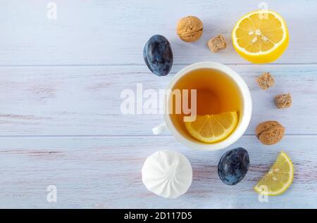 Food background with white porcelain cup of tea, lemon, ripe plums and nectarines, walnuts and white marshmallows on wooden background. Horizontal ori Stock Photo