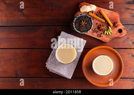 Two glasses of masala tea and various ingredients. Masala chai tea on wooden boards. Milk tea and spices. Copy space. Top view Stock Photo