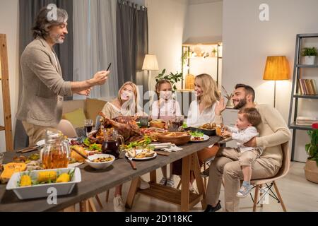Mature man with smartphone taking photo of his big family having dinner Stock Photo