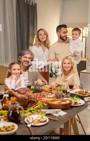 Large family of three generations sitting by table served by variety of food Stock Photo