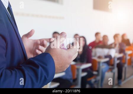 Male professor explain lesson to students and interact with them in the classroom. Selective focus on professor's hands Stock Photo
