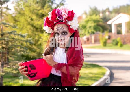 Smiling little girl in costume of halloween witch holding bucket with treats Stock Photo