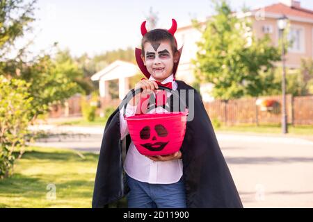 Cheerful boy in halloween costume of devil with horns on his head holding treats Stock Photo