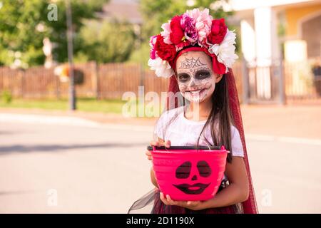 Joyful girl in costume of witch holding pink plastic bucket full of sweet treats Stock Photo