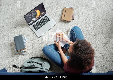 Overview of young contemporary cross-legged student having online lesson Stock Photo