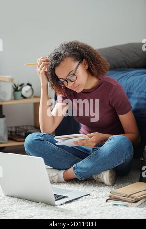 Young serious cross-legged student sitting on the floor in front of laptop Stock Photo