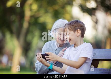 Young boy and his great grandmother using smartphone to makie video call or take selfie. Streaming online video call. Mobile internet. Watching video Stock Photo