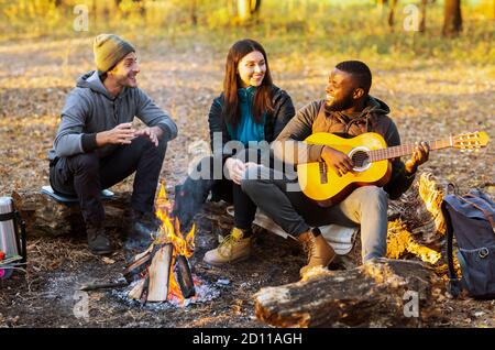 Group of friends camping and singing in autumn woods Stock Photo