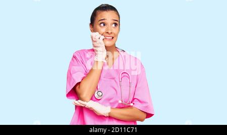 Young hispanic woman wearing doctor uniform and stethoscope looking stressed and nervous with hands on mouth biting nails. anxiety problem. Stock Photo