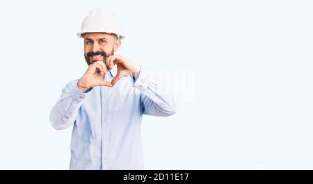 Young handsome man wearing architect hardhat smiling in love doing heart symbol shape with hands. romantic concept. Stock Photo