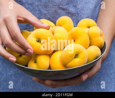 Donut Peaches in bowl held by woman with hand holding peach Stock Photo