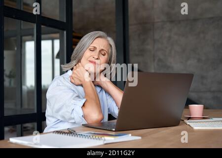 Tired stressed older mature business woman suffering from neck pain. Stock Photo
