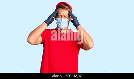 Handsome blond man with beard wearing delivery uniform and medical mask suffering from headache desperate and stressed because pain and migraine. hand Stock Photo