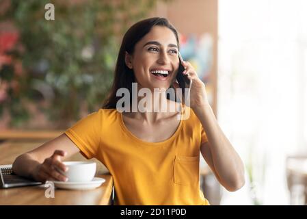 Happy lady talking on phone while drinking coffee at cafe Stock Photo