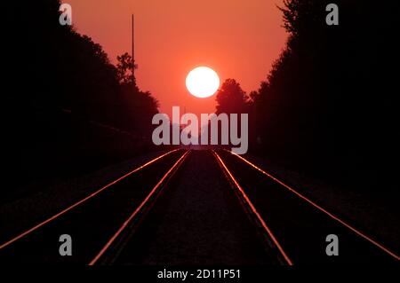 A double set of railroad tracks lead to infinity and a firey red sunset Stock Photo
